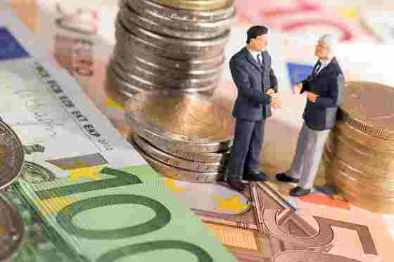 Zwei kleine Figuren stehend auf Geldscheine umringt von Münzen 